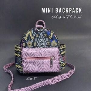 May include: A small black and pink patterned backpack with a zippered pocket and a top handle. The backpack is 8 inches in size and says "MINI BACKPACK Made in Thailand" on the front.