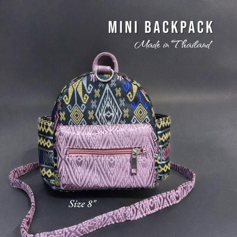 May include: A small black and pink patterned backpack with a zippered pocket and a top handle. The backpack is 8 inches in size and says "MINI BACKPACK Made in Thailand" on the front.