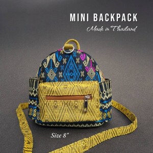 May include: A small black and gold backpack with a geometric pattern. The backpack has a zippered pocket on the front and a strap that can be adjusted. The backpack is 8 inches in size. "Mini Backpack Made in Thailand" is written on the image.