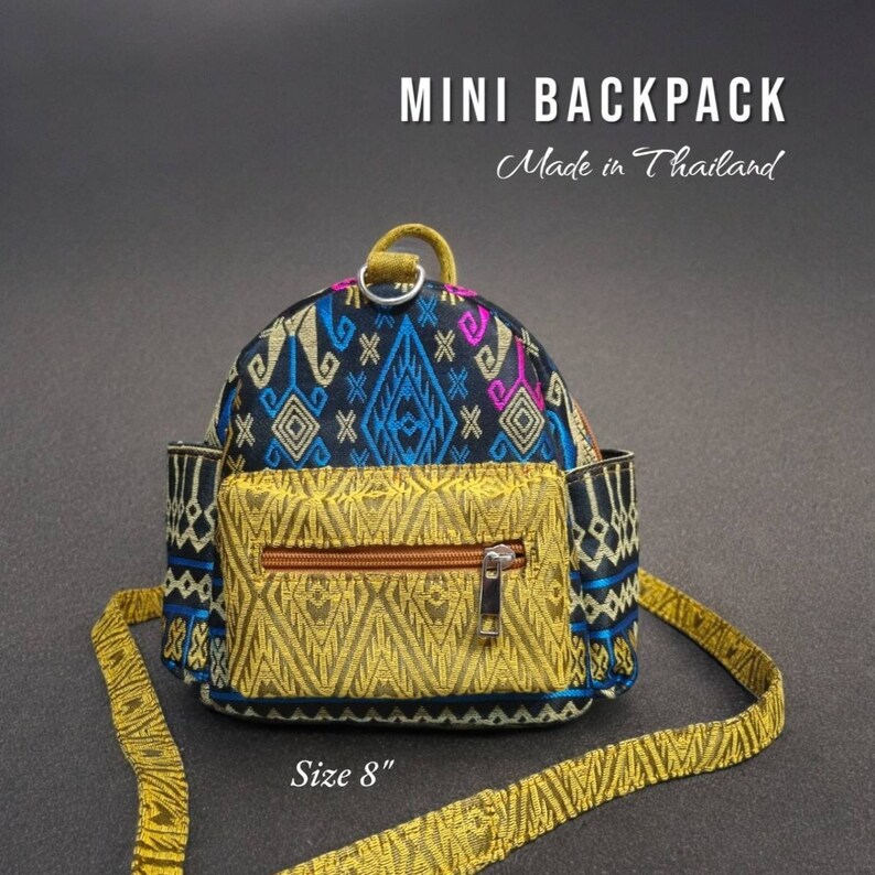 May include: A small black and gold backpack with a geometric pattern. The backpack has a zippered pocket on the front and a strap that can be adjusted. The backpack is 8 inches in size. "Mini Backpack Made in Thailand" is written on the image.