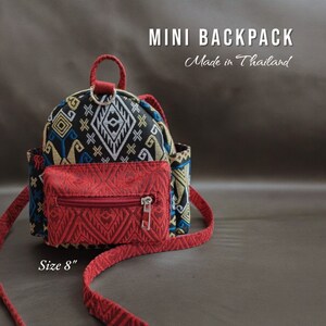 May include: A small red and black patterned backpack with a zippered pocket on the front. The backpack has a red adjustable strap and says "MINI BACKPACK Made in Thailand" and "Size 8" on the bottom.