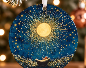 May include: A round ceramic ornament featuring a deep blue night sky with a large, glowing yellow moon and radiating golden starbursts. A small figure rests in a cradle at the bottom, surrounded by a field of shimmering golden light particles.