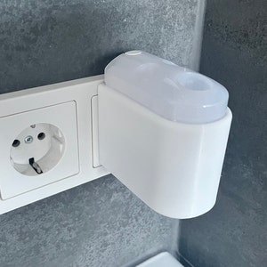 Könnte beinhalten: Eine weiße Steckdose mit einem weißen, eingesteckten Lufterfrischer.