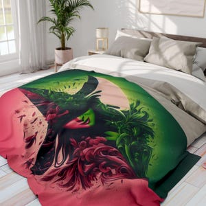 Peut inclure: Une couverture colorée avec un design vibrant représentant un visage avec une peau verte, des lèvres rouges et un chapeau noir. La couverture présente un dégradé de couleurs, dont le vert, le rouge et le rose, et est posée sur un lit avec une literie blanche et grise.