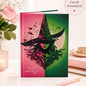 May include: A personalised journal with a split design featuring a witch illustration. The left side is pink, the right is green. The journal has the text "I Know I'm Who I Am Today Because I Knew You..." -Glinda. A pink pen and flowers are in the background.
