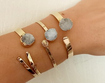 May include: Four gold bracelets with clear crystal stones. The bracelets are stacked on a person's wrist.