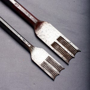 Peut inclure: Deux ciseaux à bois anciens en métal. Les ciseaux ont une tête rectangulaire avec des rainures parallèles et une extrémité pointue. Les manches sont de couleur brun rougeâtre foncé. Aspect vieilli.