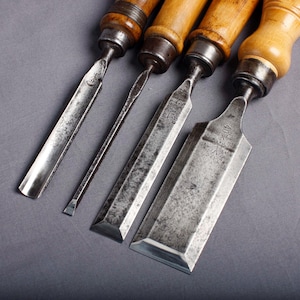 May include: Four vintage wood chisels with wooden handles and metal blades. The chisels are arranged diagonally, showcasing their different blade shapes and sizes. The metal blades have a worn, aged appearance, suggesting use over time.