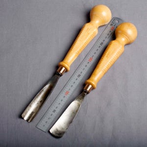 K&ouml;nnte beinhalten: Zwei Holzschnitzgouge mit hellen Holzgriffen und Metallklingen, neben einem Metalllineal. Das Lineal zeigt Messungen bis zu 300 mm. Die Gouges haben eine kupferfarbene Zwinge.