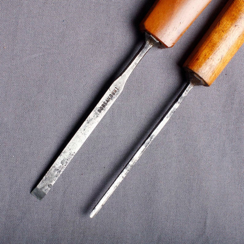 Peut inclure: Deux ciseaux &agrave; bois avec des manches en bois et des lames en m&eacute;tal. L'un des ciseaux porte l'inscription "BORSAKOSKI" grav&eacute;e sur la lame. Les outils sont pos&eacute;s sur un fond gris.