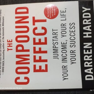 May include: A white book with a red title that reads "The Compound Effect: Jumpstart Your Income, Your Life, Your Success". The author is Darren Hardy, publisher of Success magazine.