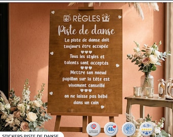 May include: A wooden sign on an easel with the text "Piste de danse" and other French text. The sign is decorated with small white hearts. The sign is surrounded by floral arrangements and decorative items.