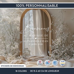 Peut inclure: Miroir doré avec l'inscription "Bienvenue" et "Au Mariage de Alexandra & Jean 18 Avril 2026" en écriture blanche. Le miroir est entouré de fleurs blanches. Le texte "100% PERSONNALISABLE" est en haut.