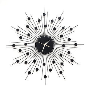 Könnte beinhalten: Schwarze Wanduhr aus Metall mit Sonnenstrahl-Design. Das Zifferblatt der Uhr ist schwarz mit goldenen Stunden- und Minutenzeigern.