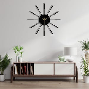 Puede incluir: Un reloj negro con agujas doradas y fondo negro. El reloj tiene un dise&ntilde;o moderno con radios negros delgados que irradian desde el centro.