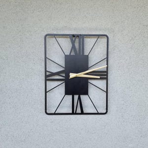 May include: Black metal wall clock with Roman numeral markings and gold-colored hands.