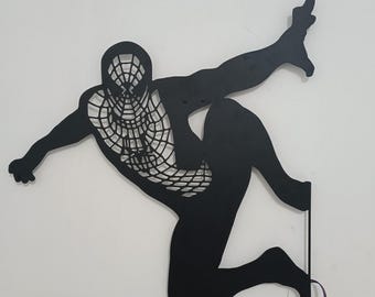 May include: Black metal wall art depicting a superhero in a webbed suit, posed in a dynamic action pose. The art piece is lit from behind, creating a dramatic silhouette effect.