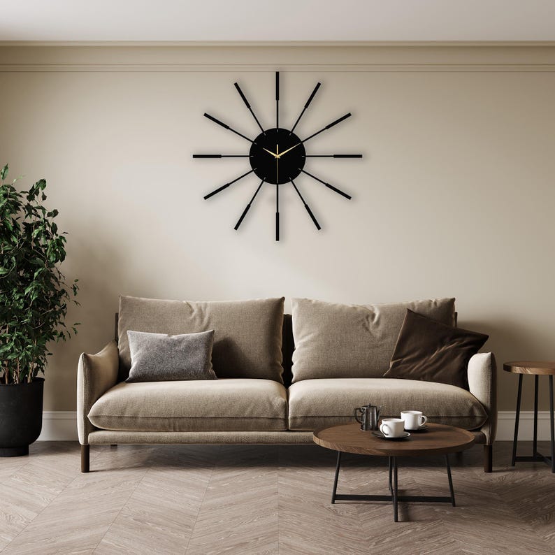 Puede incluir: Un reloj negro y dorado con un dise&ntilde;o de rayos de sol cuelga de una pared beige sobre un sof&aacute; beige con almohadas marrones. Una mesa de caf&eacute; marr&oacute;n se encuentra frente al sof&aacute;.