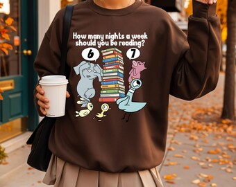 Puede incluir: Una sudadera marrón con el texto "How many nights a week should you be reading?" e ilustraciones de animales y libros. El diseño incluye un elefante, un cerdo, una paloma y otros pájaros, con los números 6 y 7.
