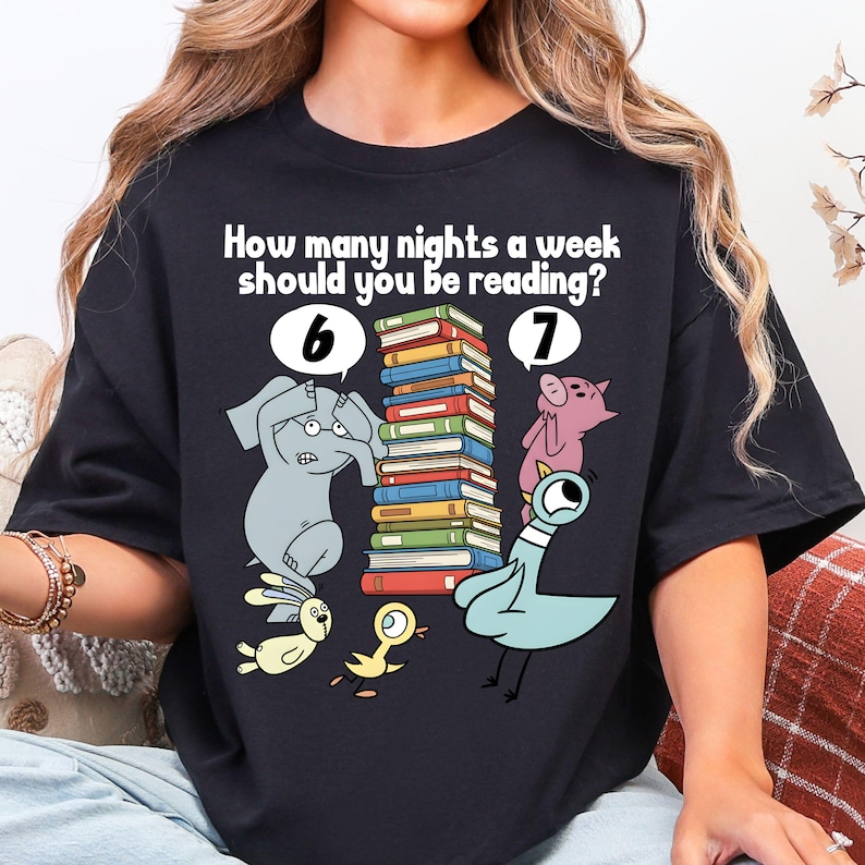 May include: Black t-shirt with the text "How many nights a week should you be reading?" and illustrations of an elephant, pig, pigeon, and other animals. The design includes a stack of books and the numbers 6 and 7.