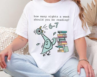 Puede incluir: Camiseta blanca con un diseño de paloma de dibujos animados y el texto "how many nights a week should you be reading?" y "6-7". También se muestra una pila de libros. La camiseta es de estilo casual y cómodo.