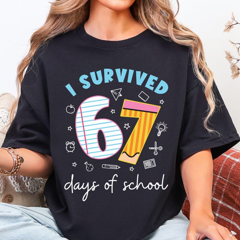 May include: Black t-shirt with the text "I SURVIVED 67 days of school." The number 67 is designed with a notebook and pencil. The shirt has a crew neck and short sleeves.