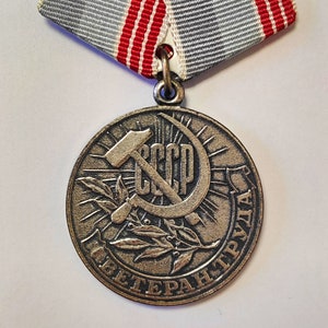 以下が含まれることがあります： ハンマーと鎌、月桂樹の輪、そして「CCCP ВЕТЕРАН ТРУДА」（ソ連労働功労者）という文字が刻まれたブロンズ製のメダル。メダルはグレーとレッドのリボンで飾られています。