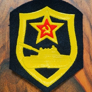 May include: A black felt patch with a yellow border and a yellow tank silhouette. A red star with a hammer and sickle inside is above the tank.