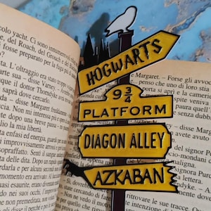 May include: A black and yellow metal bookmark with the words "Hogwarts", "Platform 9 3/4", "Diagon Alley", and "Azkaban". A white owl sits atop the bookmark, which is placed in an open book.