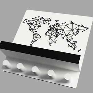 May include: A white key holder with a black geometric world map design. The key holder has a black shelf and five white pegs for hanging keys. The design is modern and minimalist.