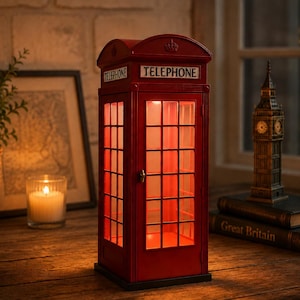 May include: A bright red, illuminated model of a British telephone box featuring a grid-patterned door, a small metal handle, and the word TELEPHONE printed in black lettering on a white background above the door and on the side panels.