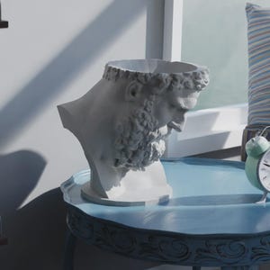 Könnte beinhalten: Eine weiße Büste eines bärtigen Mannes auf einem hellblauen Tisch. Ein mintgrüner Wecker und ein gestreiftes Kissen sind ebenfalls zu sehen. Die Büste ist ein dekorativer Gegenstand. Der Tisch ist wahrscheinlich aus Holz.