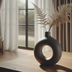 以下が含まれることがあります： 丸い開口部のあるモダンなマットブラックの花瓶。乾燥した観賞用の草が入っています。花瓶は明るい木製のテーブルの上にあり、窓から自然光が差し込んでいます。家の装飾。
