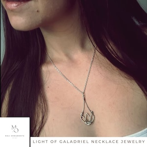 May include: A silver necklace with a delicate pendant shaped like a stylized flower. The pendant is made of wire and has a small, clear stone in the center. The necklace is worn by a person with long, dark hair.