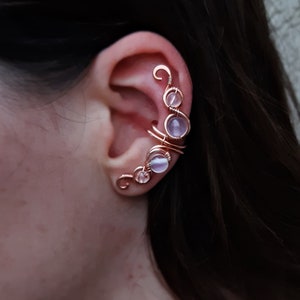 May include: Rose gold ear cuff with a delicate wire design and four pale pink gemstones.