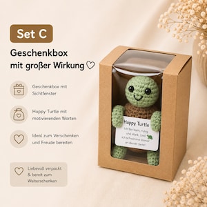 May include: A crocheted green turtle with a brown shell is displayed in a clear-windowed cardboard gift box. The turtle holds a card with text. The box is part of a gift set, as indicated by the text "Set C".