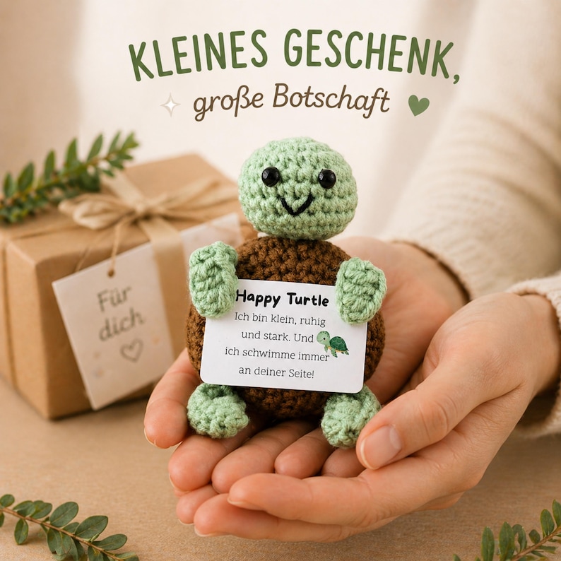 May include: A crocheted turtle figurine with a green head and limbs, and a brown shell, holding a card that reads "Happy Turtle". The image also shows a wrapped gift box with a tag that says "For you". Text at the top says "KLEINES GESCHENK, gro&szlig;e Botschaft".