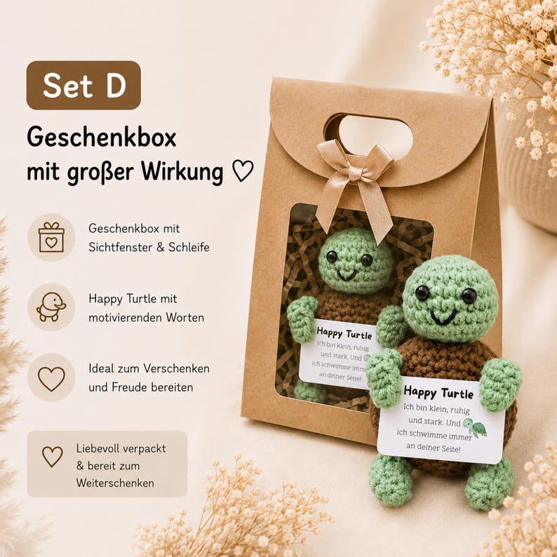 May include: A brown paper gift bag with a window, tied with a bow, contains a crocheted green and brown turtle. The turtle holds a sign that reads "Happy Turtle". The text "Set D" and "Geschenkbox mit gro&szlig;er Wirkung" are also visible.