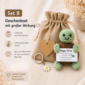 May include: A gift set featuring a crocheted turtle with a sign that reads "Happy Turtle". The set includes a jute bag, a daisy keychain, and a heart-shaped tag. The turtle is green and brown.