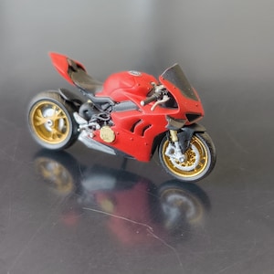 Peut inclure: Une moto jouet rouge et noire avec des roues dorées. La moto est une réplique d'une Ducati.