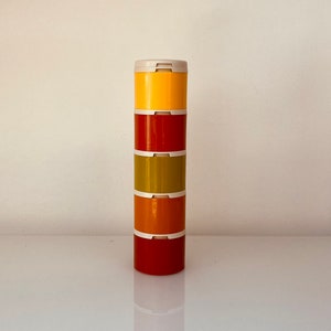 May include: A stack of four colorful canisters with white lids. The canisters are yellow, red, green, and orange.