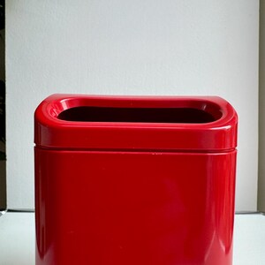 Puede incluir: Un recipiente rectangular rojo brillante con una abertura superior redondeada. El recipiente tiene un acabado liso y brillante y un interior oscuro. El dise&ntilde;o es simple y moderno, adecuado para diversos usos.