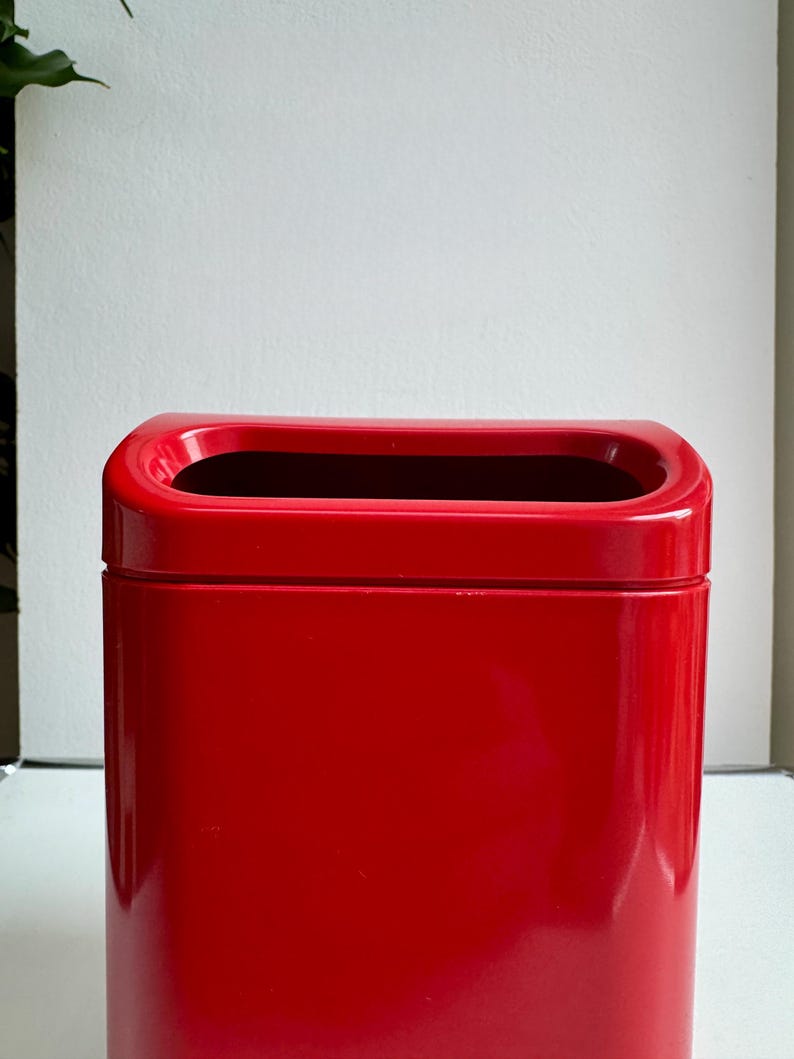 Puede incluir: Un recipiente rectangular rojo brillante con una abertura superior redondeada. El recipiente tiene un acabado liso y brillante y un interior oscuro. El dise&ntilde;o es simple y moderno, adecuado para diversos usos.