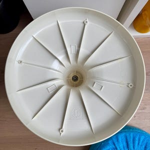 May include: Off-white plastic chair base with a radial spoke design. The base has a central hub with a metal component and several rectangular and circular openings. A blue fabric cushion is visible in the lower right corner.
