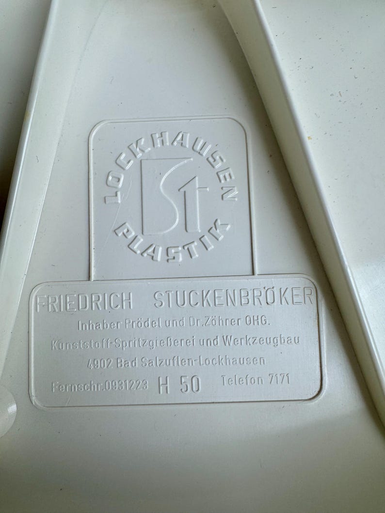 May include: Close-up of a white plastic object with embossed text. The text includes the name "LOCKHAUSEN PLASTIK" in a circular design and "FRIEDRICH STUCKENBR&Ouml;KER" with additional details about the manufacturer.