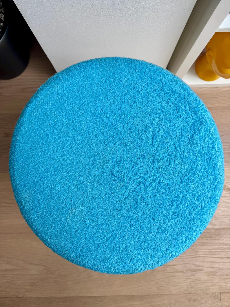 May include: A round, bright turquoise rug with a soft, textured surface. The rug is circular and appears to be made of a plush material. The rug is placed on a light-colored wooden floor.