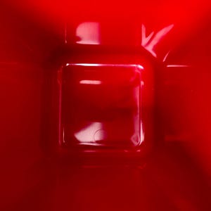Puede incluir: Primer plano de una superficie roja brillante y brillante con una hendidura cuadrada en el centro. La hendidura tiene forma rectangular con esquinas redondeadas. La iluminaci&oacute;n crea reflejos y sombras, enfatizando la textura.