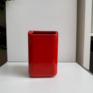 Puede incluir: Un recipiente rectangular rojo brillante con esquinas redondeadas y acabado brillante. El interior es negro. El recipiente est&aacute; sobre una superficie blanca.