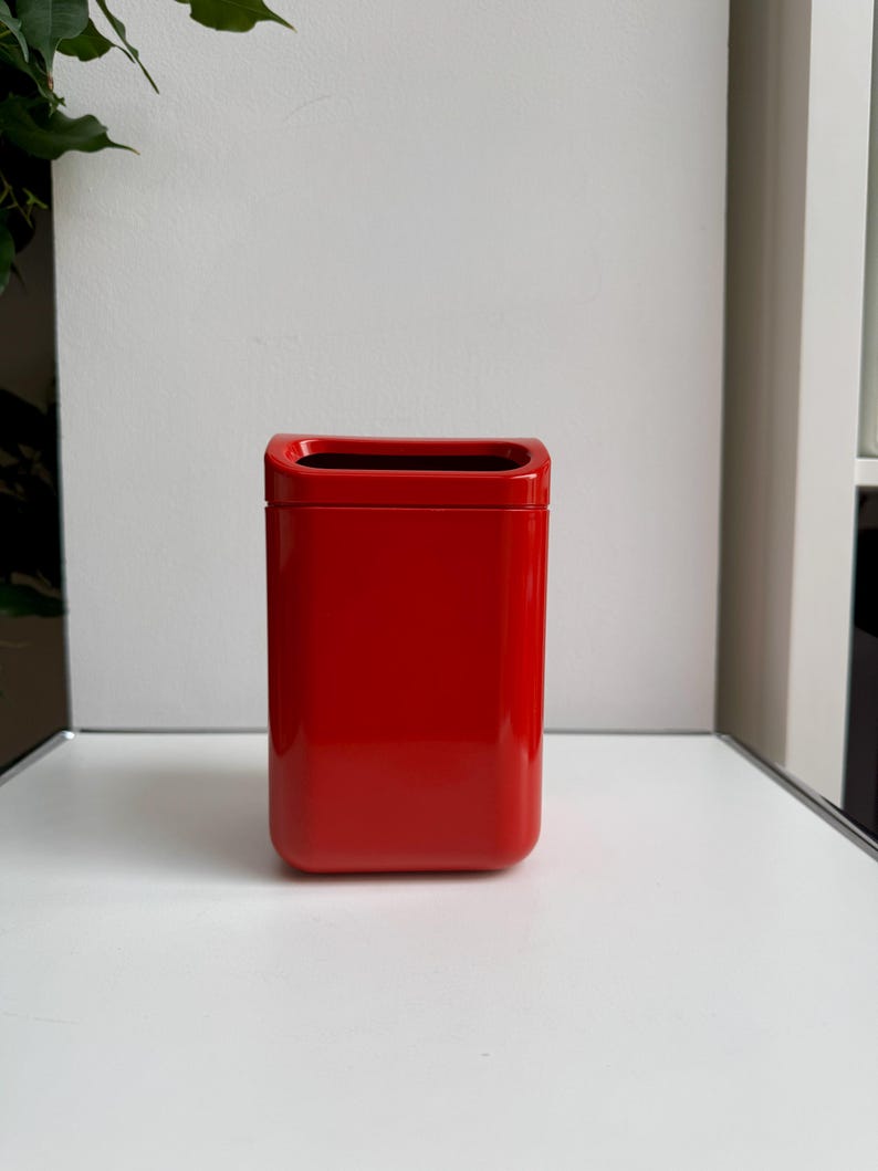 Puede incluir: Un recipiente rectangular rojo brillante con esquinas redondeadas y acabado brillante. El interior es negro. El recipiente est&aacute; sobre una superficie blanca.