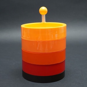 Può includere: Un contenitore impilabile in plastica arancione, rosso e nero con un piccolo pomello arancione in cima.